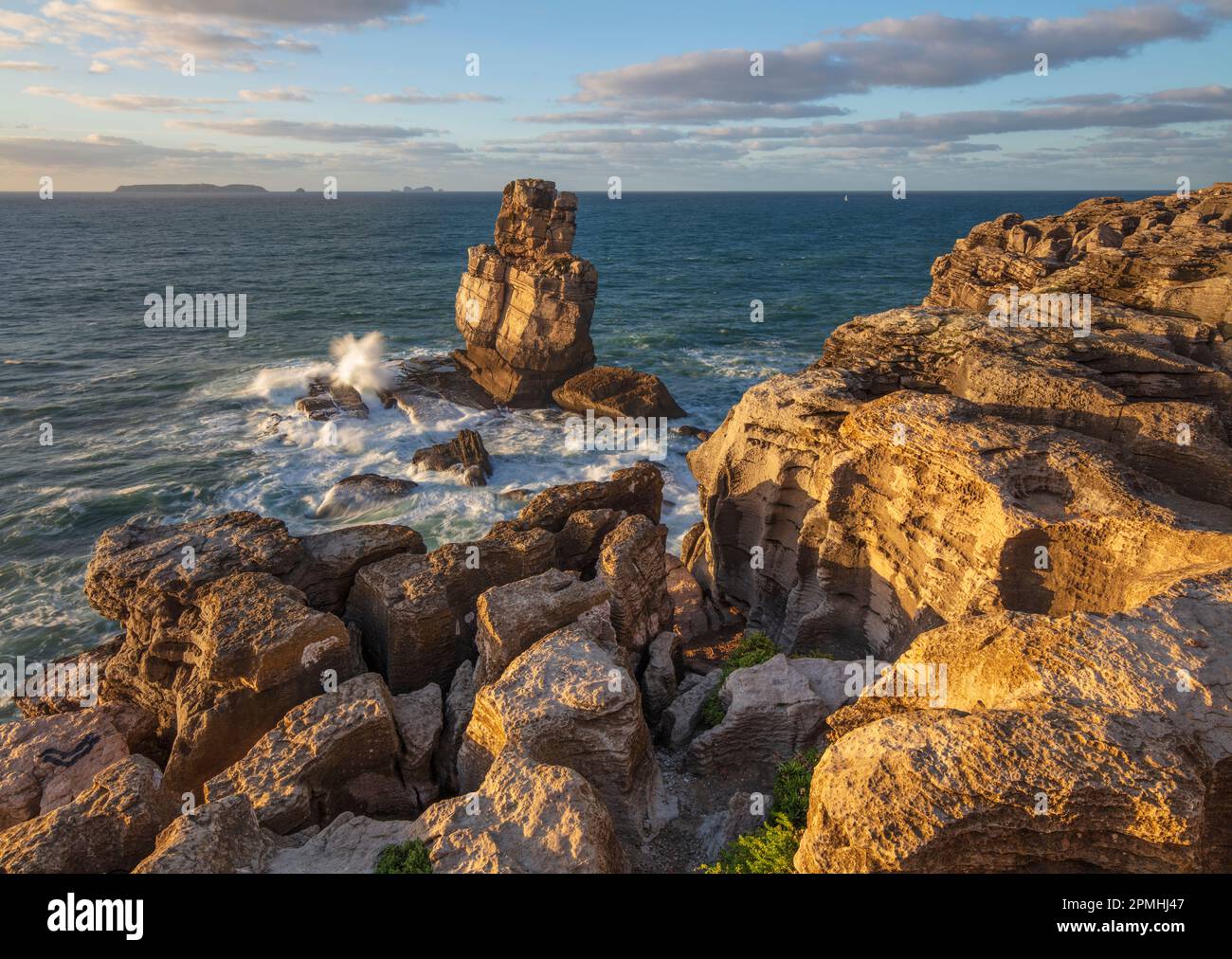 Onde che si schiantano contro lo stack roccioso a Cabo Carvoeiro alla luce del sole serale con Ilha da Berlenga in lontananza, Peniche, Regione Centro Foto Stock