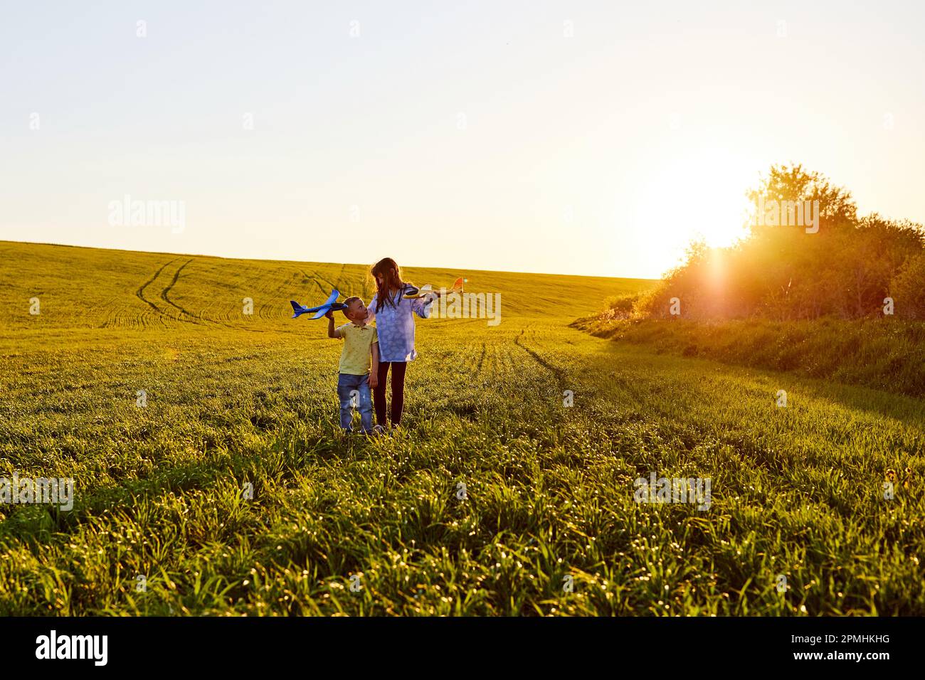 Running boy and girl holding due aerei gialle e blu giocattolo nel campo durante il tramonto estivo Foto Stock