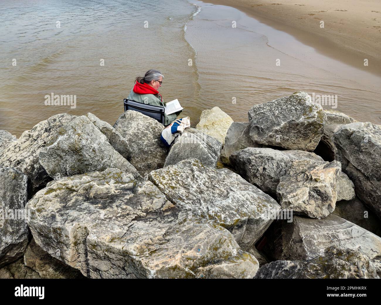 Donna che legge un libro sulla roccia della spiaggia Foto Stock