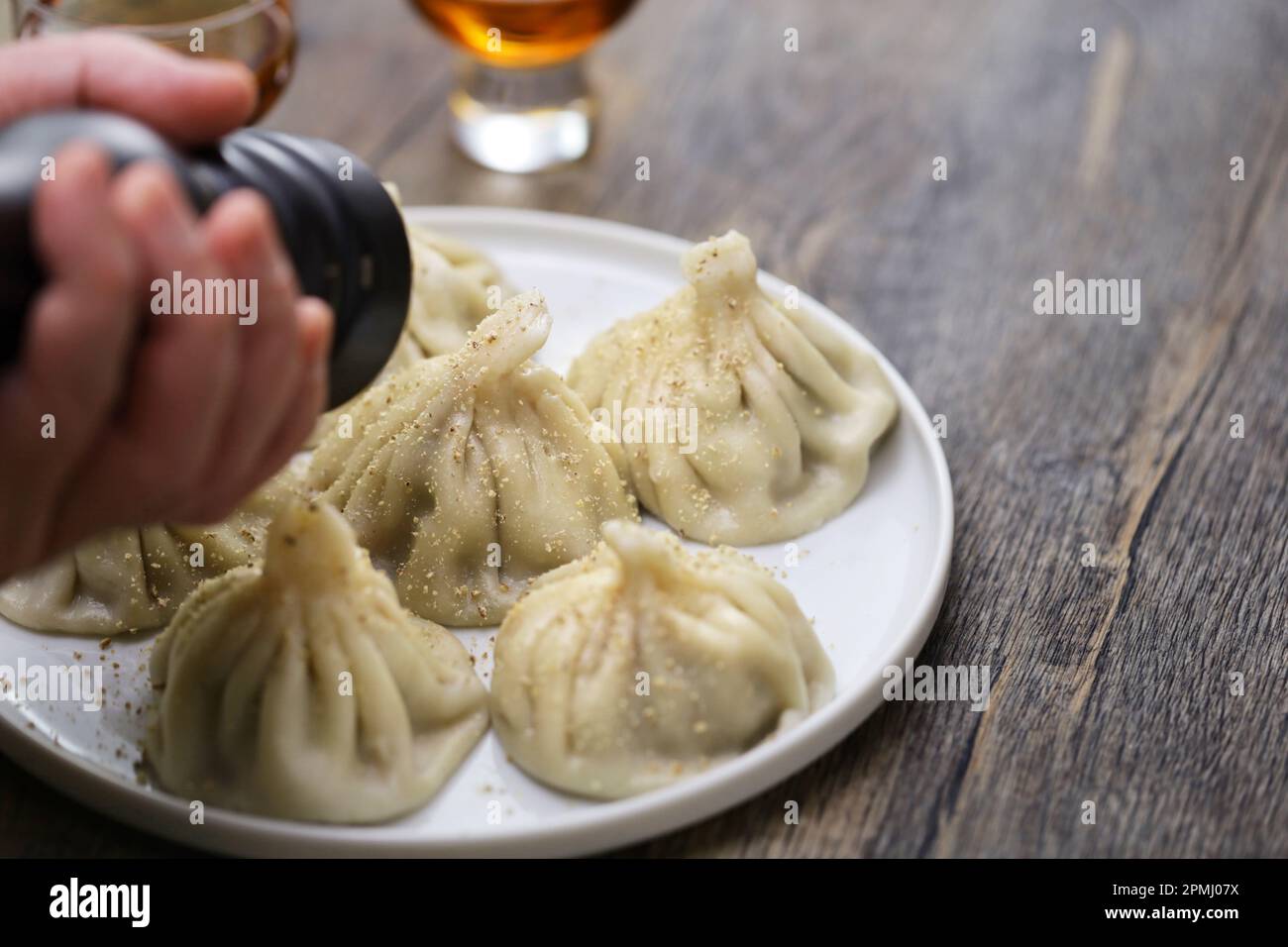 Macinare i grani di pepe nero con un mulino a pepetti su gnocchi di Khinkali fatti in casa, cibo tradizionale georgiano Foto Stock