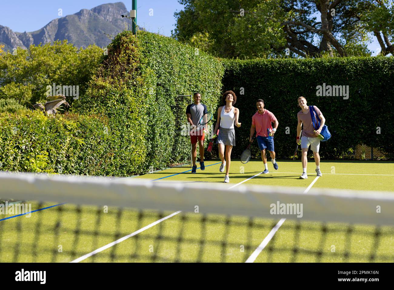 Felice gruppo variegato di amici che arrivano insieme al campo da tennis Foto Stock