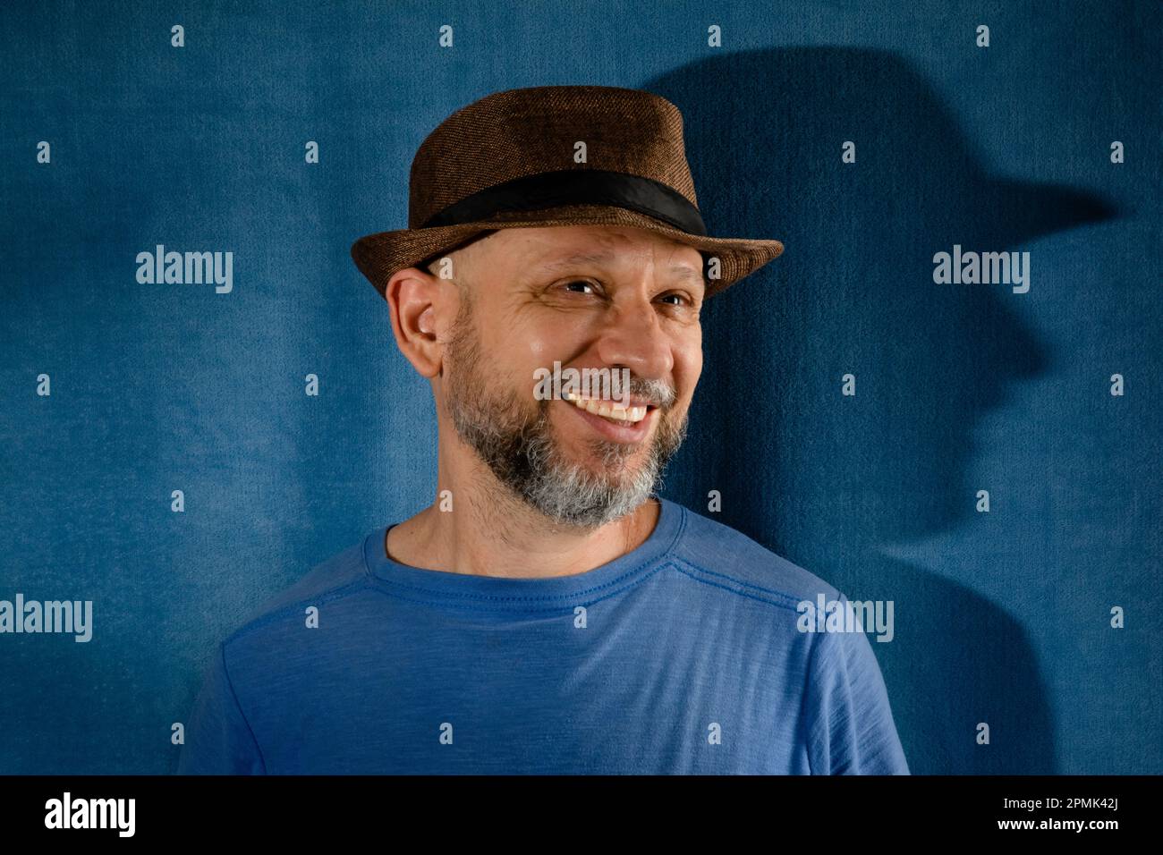 Uomo sorridente che indossa un cappello. Isolato su sfondo blu con ombra. Foto Stock