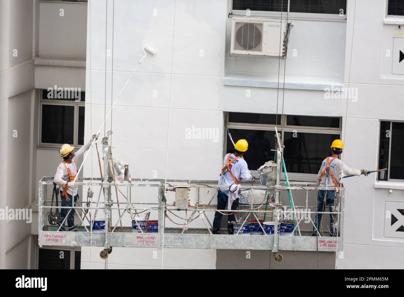 Il sollevatore per ponteggi con tre pittori esperti applica un nuovo strato di vernice chimica sulla facciata esterna dell'alloggiamento per dare un aspetto pulito al marchio. Singapore. Foto Stock