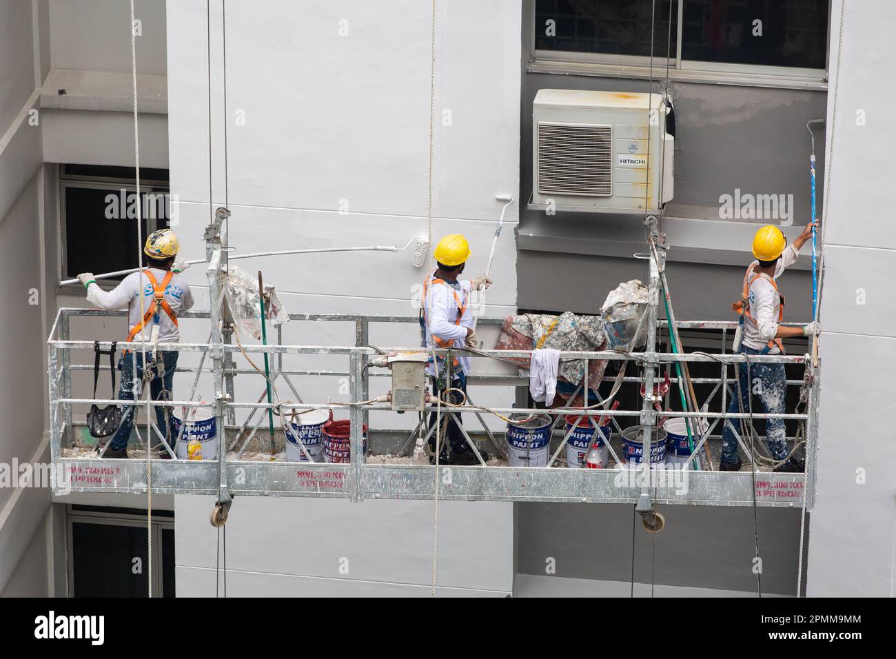 Tre lavoratori con casco di sicurezza su ponteggio ascensore dipingere vernice fresca sul esterni architettura. Foto Stock