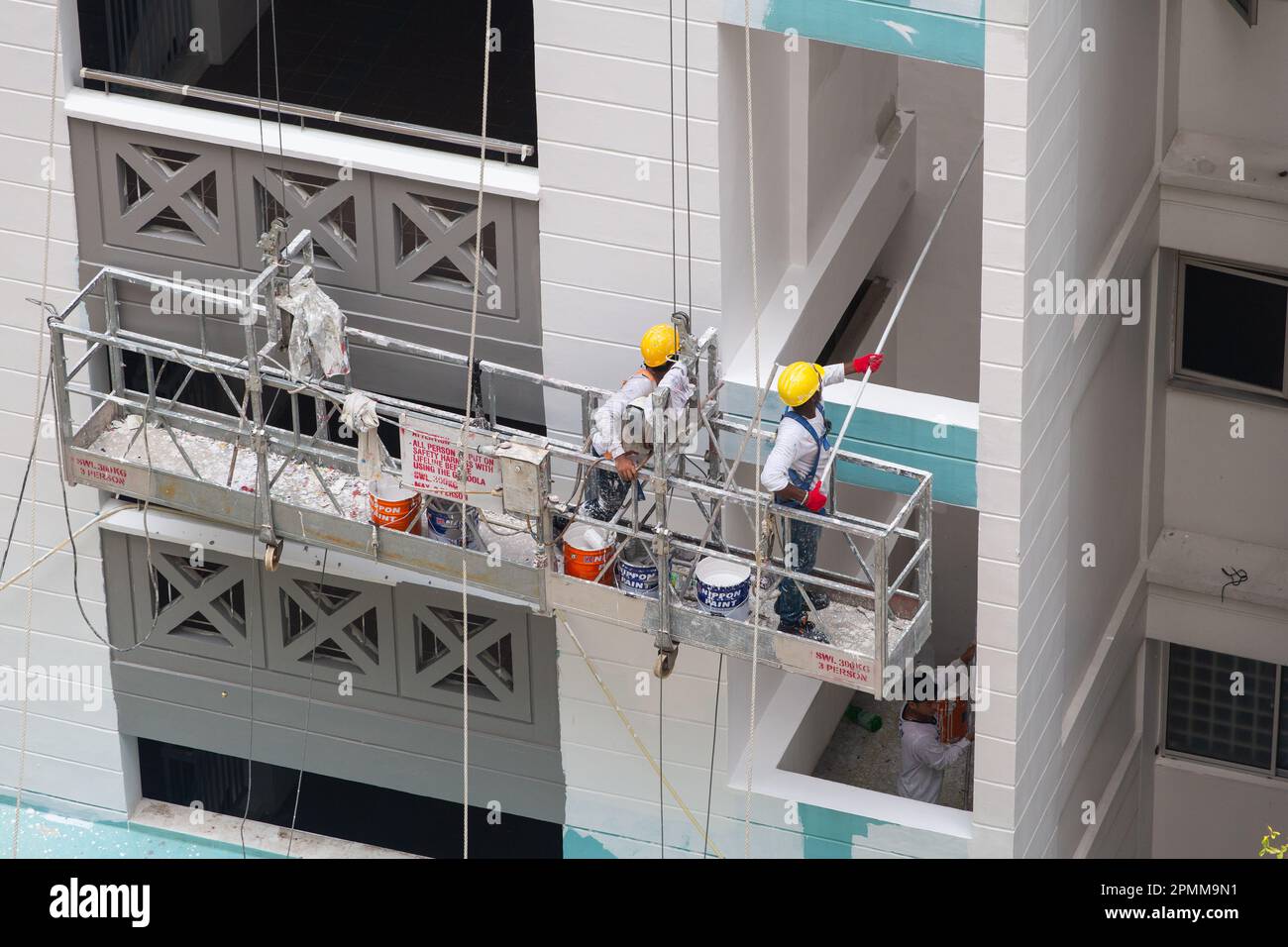 Due pittori su ponteggi ascensore pittura fresca di vernice bianca sull'esterno dell'edificio. Foto Stock