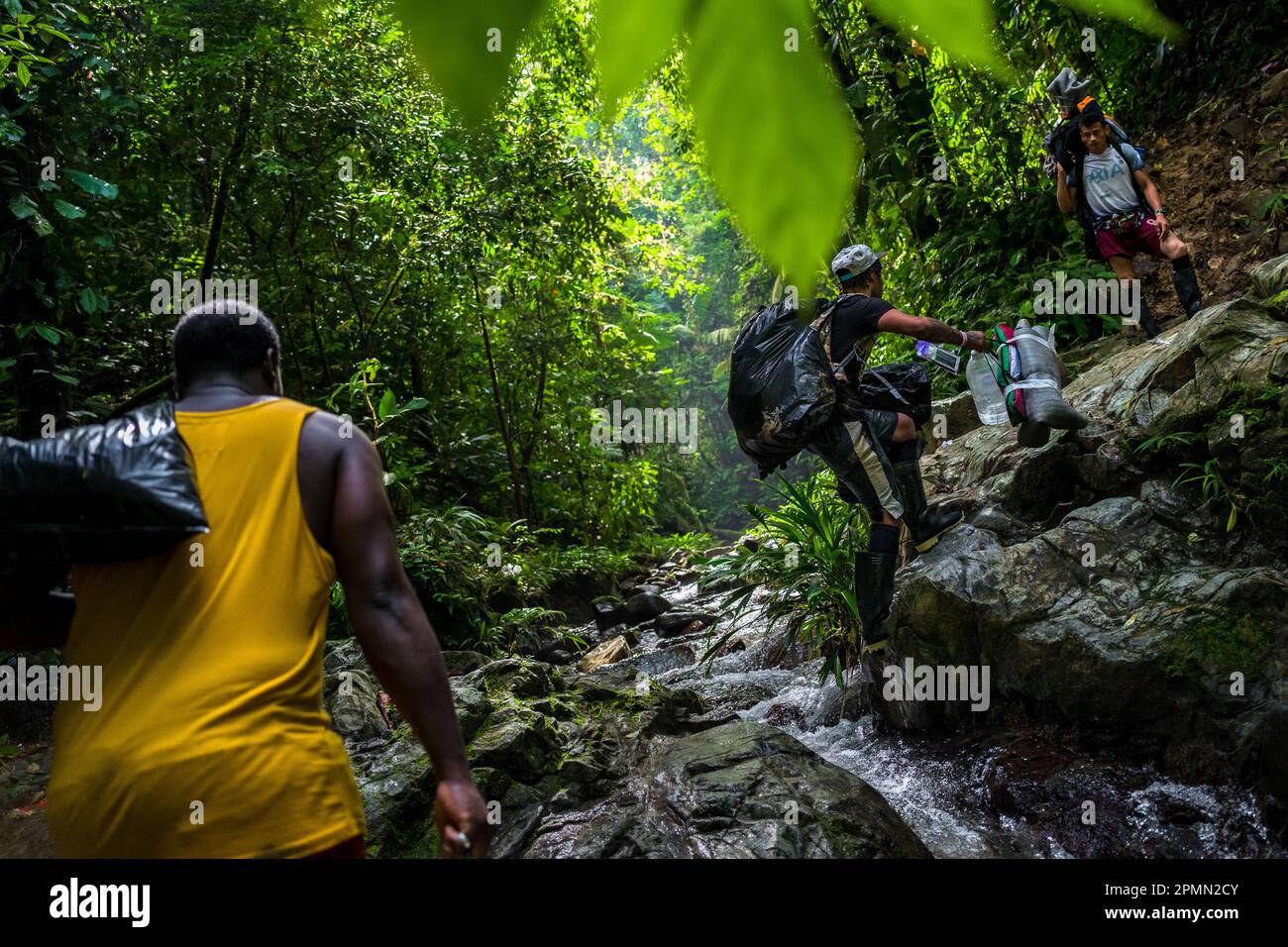 I migranti provenienti dall'Ecuador attraversano un torrente mentre si arrampicano su un sentiero roccioso nella selvaggia e pericolosa giungla del Darién Gap tra Colombia e Panamá. Foto Stock