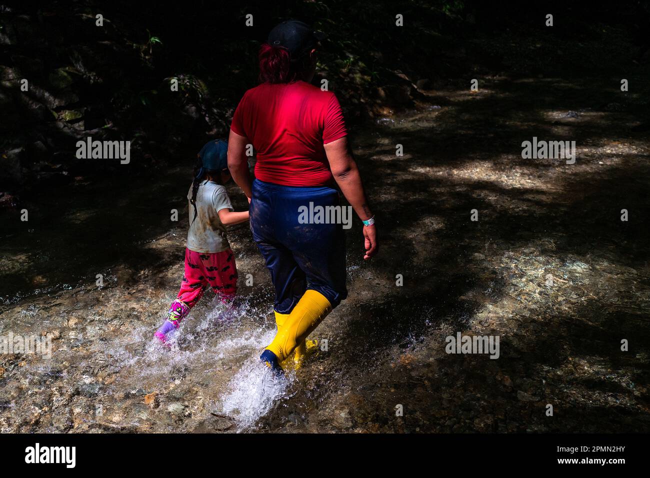 Un immigrato ecuadoriano, accompagnando sua figlia, cammina attraverso il fiume nella pericolosa giungla del Darién Gap tra Colombia e Panamá. Foto Stock