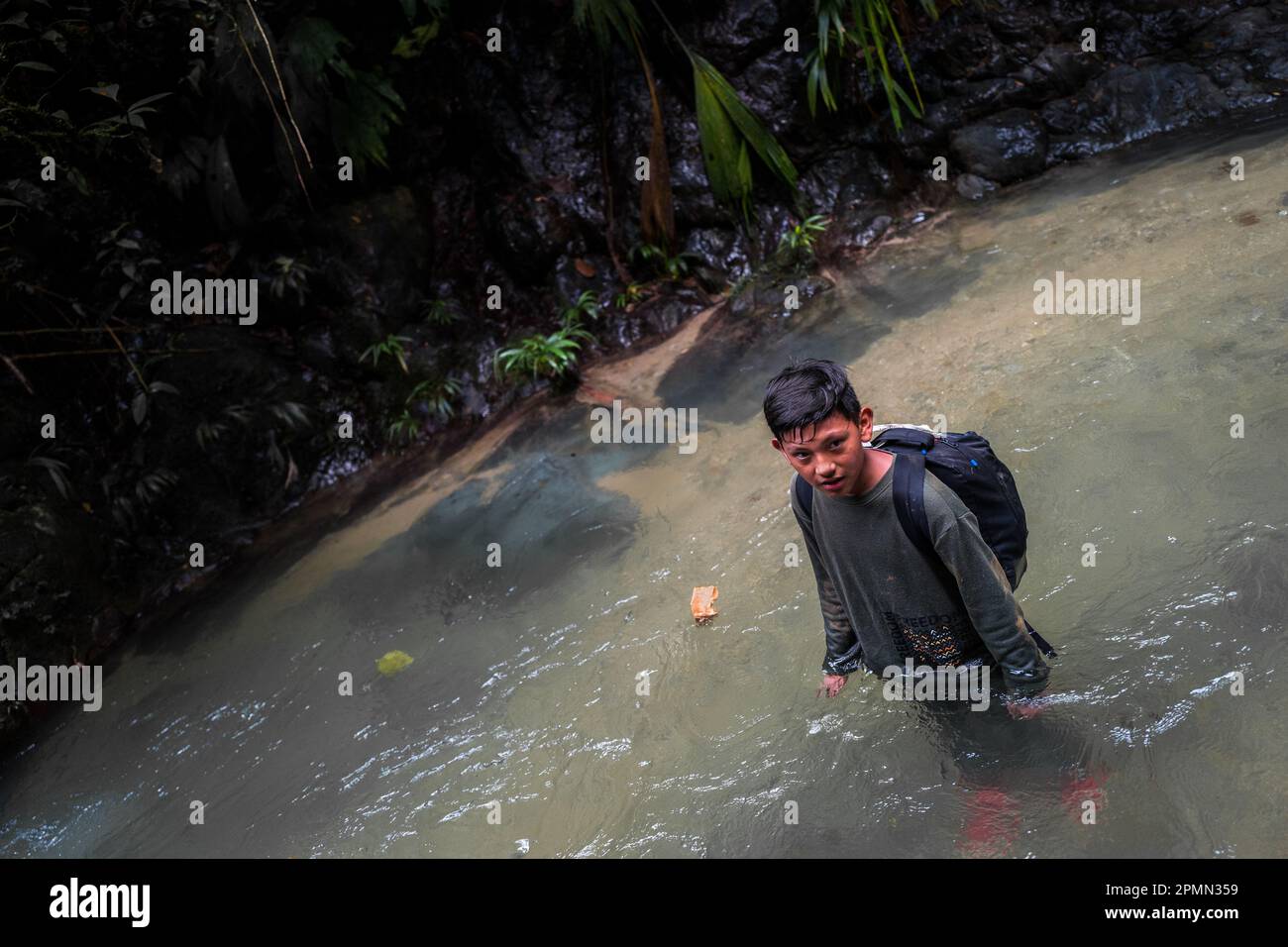Un bambino migrante sta in piedi in acqua mentre guado il fiume nella giungla selvaggia e pericolosa del Darién Gap tra Colombia e Panamá. Foto Stock