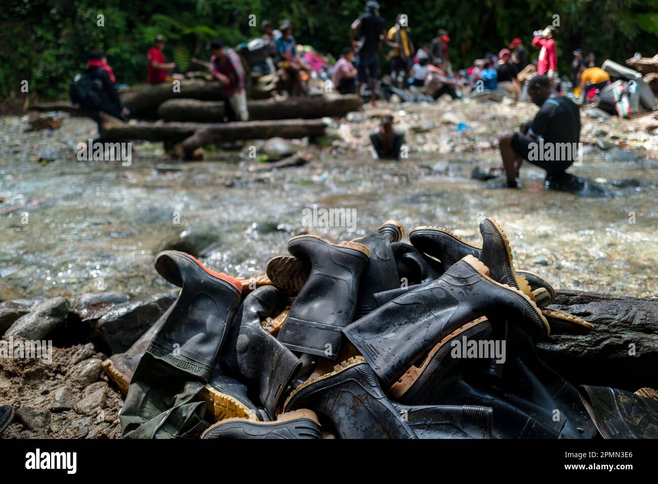 Un mucchio di stivali di gomma usurati, scartati dai migranti, si trova sulla riva del fiume nella giungla del Darién Gap tra Colombia e Panamá. Foto Stock
