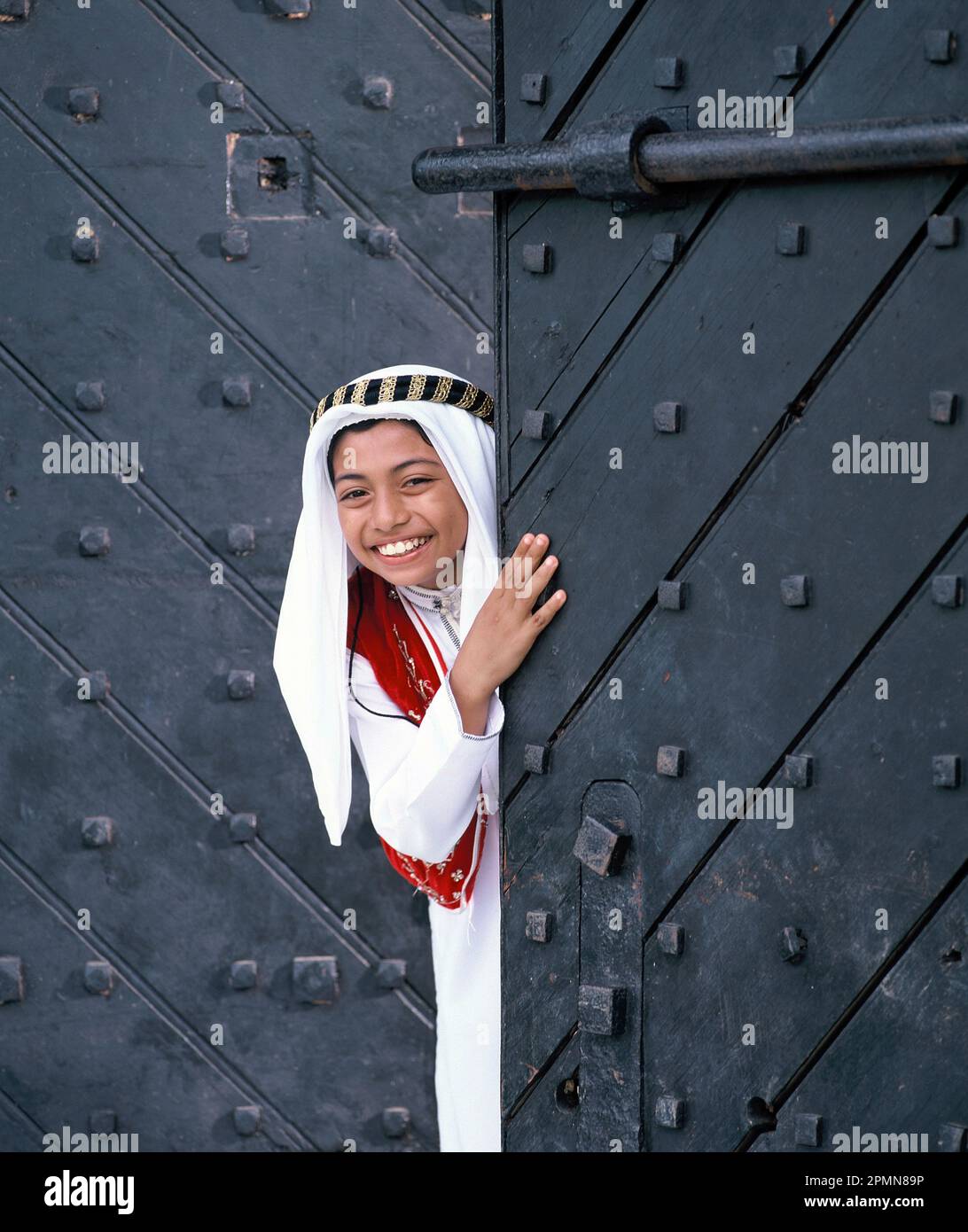 Singapore. Ragazzo arabo che si affaccia da antiche porte in legno massiccio. Foto Stock