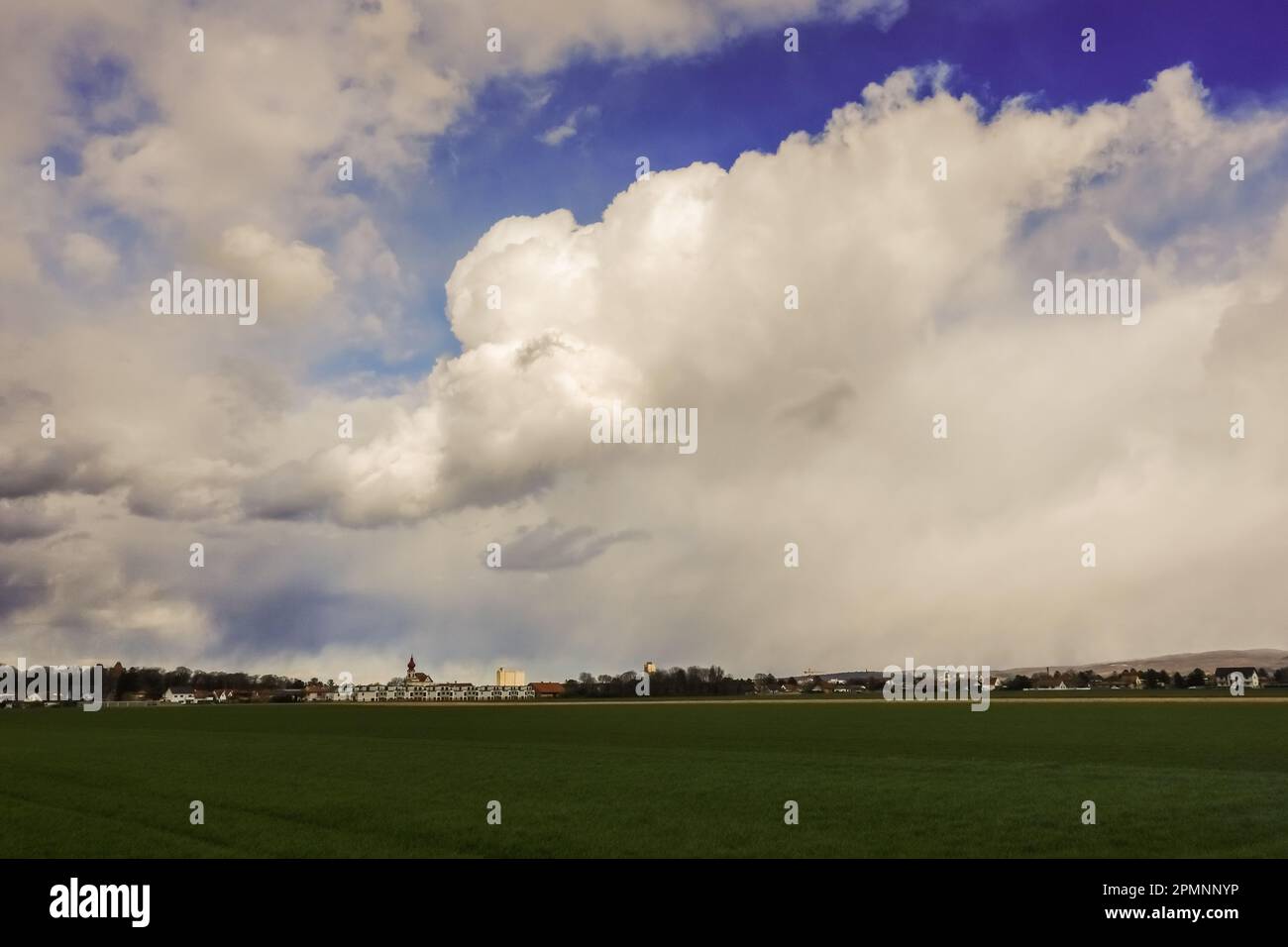 dense nuvole bianche e grigie sul cielo blu sopra un villaggio e campi in primavera Foto Stock
