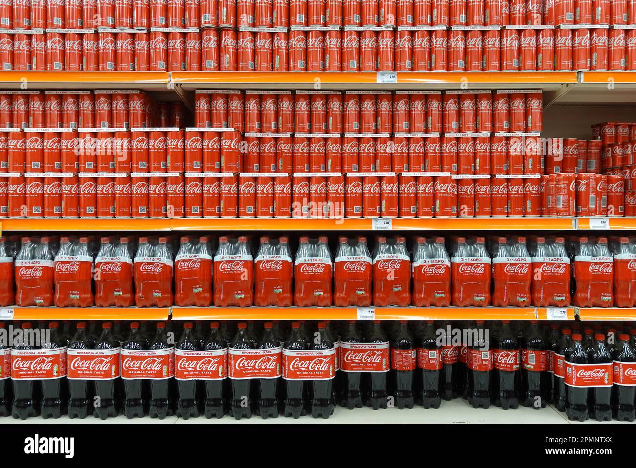 Atene, Grecia - 6 marzo 2023: Scaffali impilati con lattine e bottiglie per bibite analcoliche Coca Cola di varie dimensioni. Foto Stock