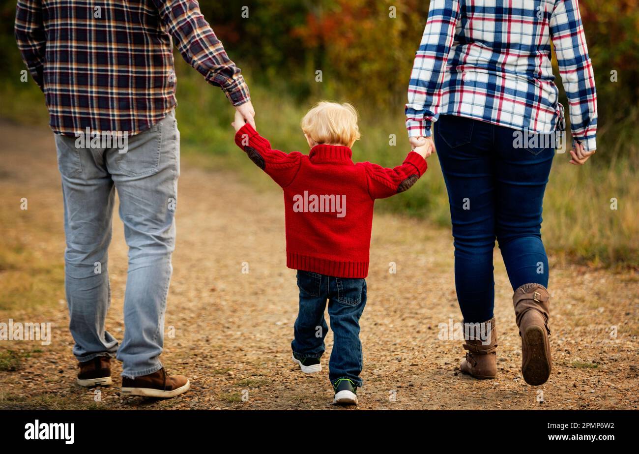 Madre e padre si tengono per mano con il figlio più piccolo mentre camminano lungo un sentiero in un parco cittadino in autunno; Edmonton, Alberta, Canada Foto Stock