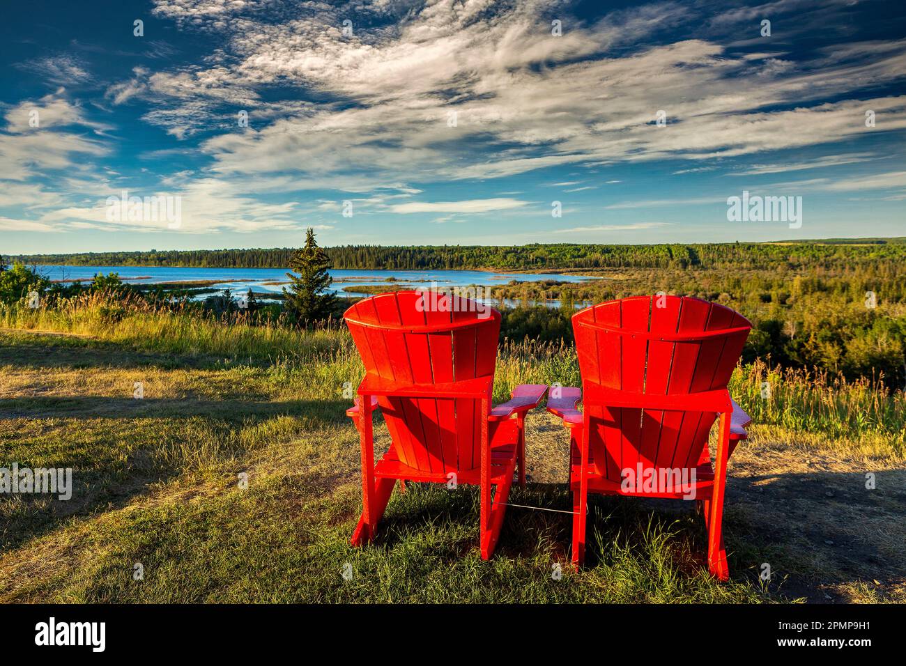 Due grandi sedie rosse con luce calda al tramonto su un campo che si affaccia su una valle del fiume con nuvole spettacolari e cielo blu; Calgary, Alberta, Canada Foto Stock