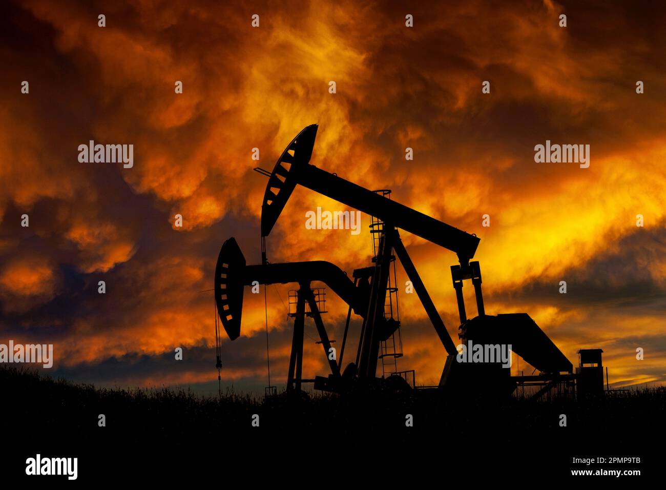 Silhouette di due pompe all'alba con spettacolari nuvole luminose e colorate sullo sfondo, a ovest di Airdrie; Alberta, Canada Foto Stock