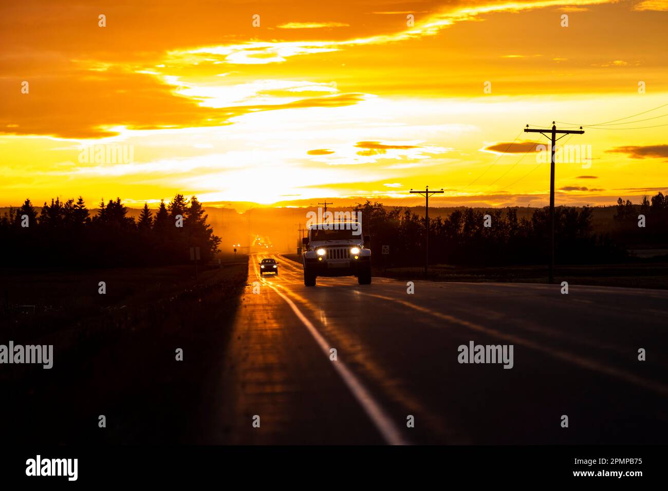 Veicoli su un'autostrada rurale al tramonto; Alcomdale, Alberta, Canada Foto Stock