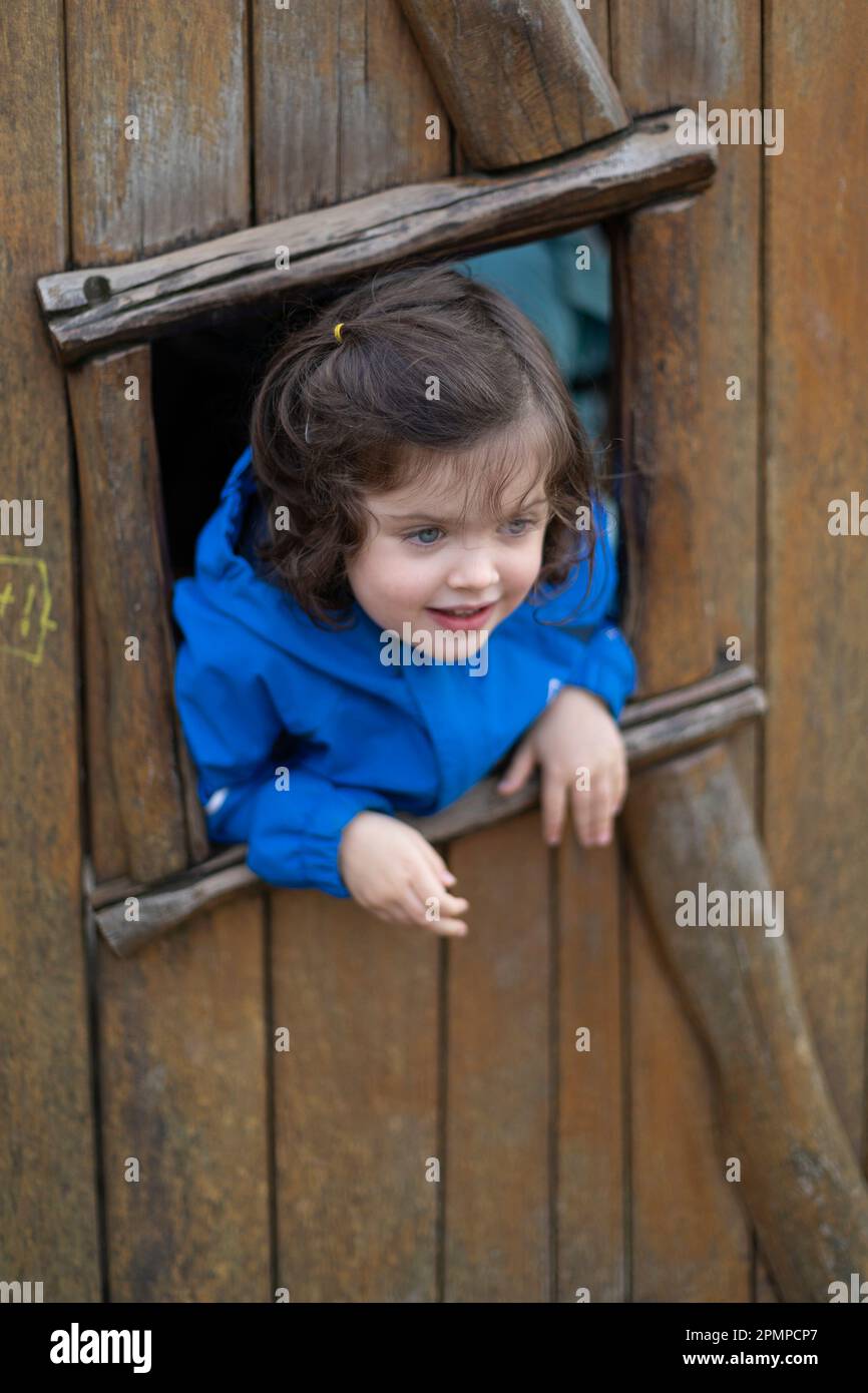 Bambina in età prescolare che guarda fuori dalla finestra di una casa sull'albero; West Vancouver, British Columbia, Canada Foto Stock