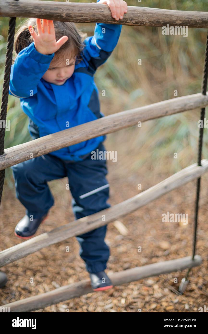Una bambina in età prescolare sale una scala mentre gioca in un parco giochi; West Vancouver, British Columbia, Canada Foto Stock