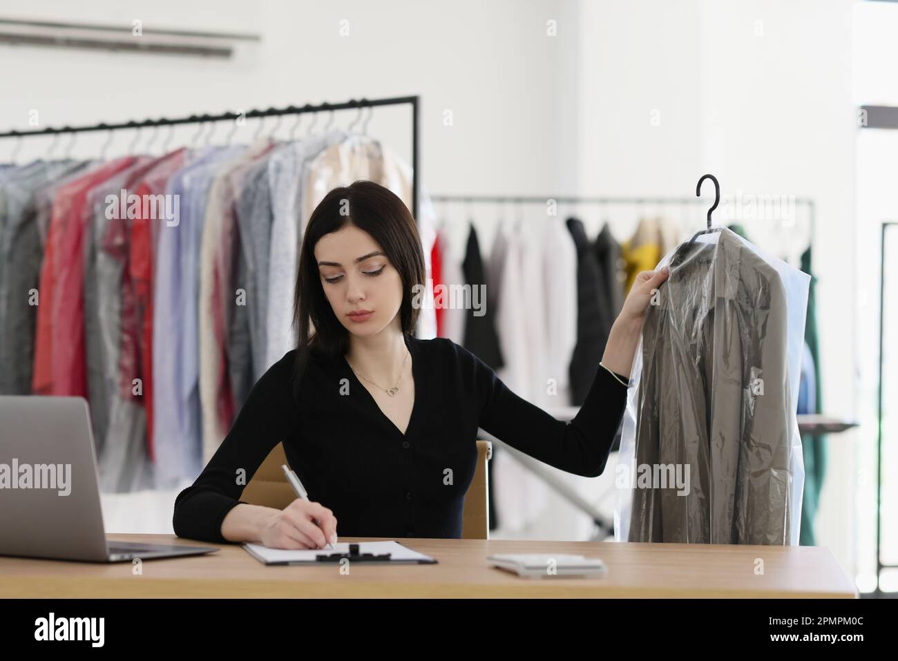 La donna prende appunti sulla clipboard che tiene il cappotto sotto la pellicola Foto Stock