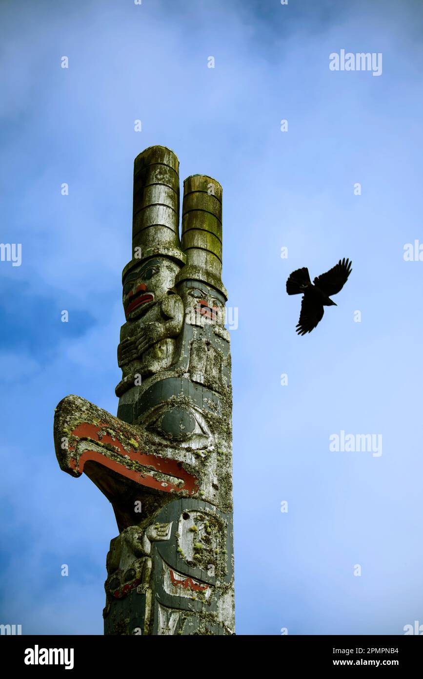 Parte superiore di un totem con un corvo che vola sullo sfondo a Old Massett, una comunità di Haida sull'isola Graham Foto Stock