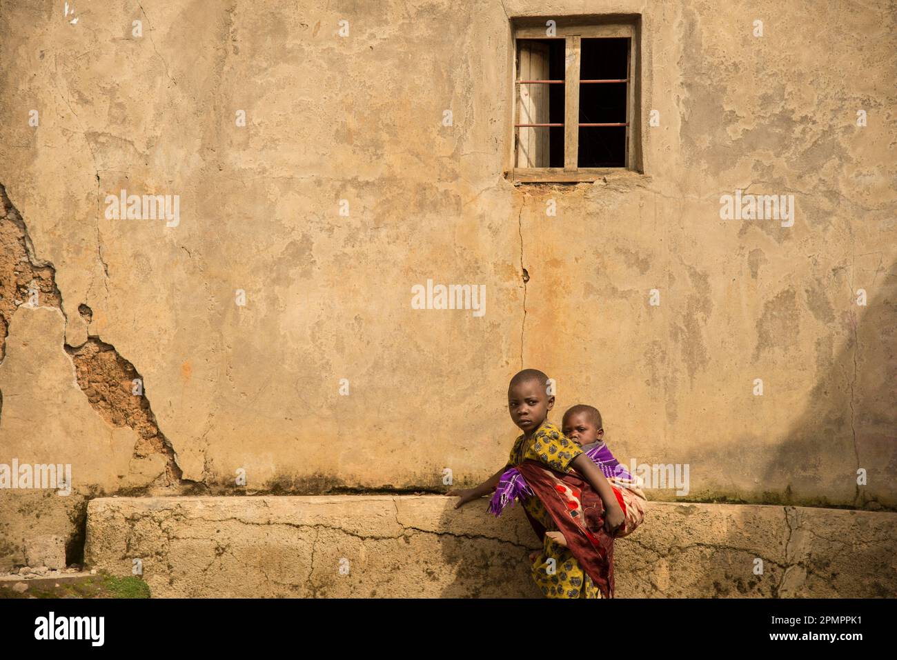 Bambino più grande che porta un giovane sulla schiena vicino a un muro; Ruanda Foto Stock
