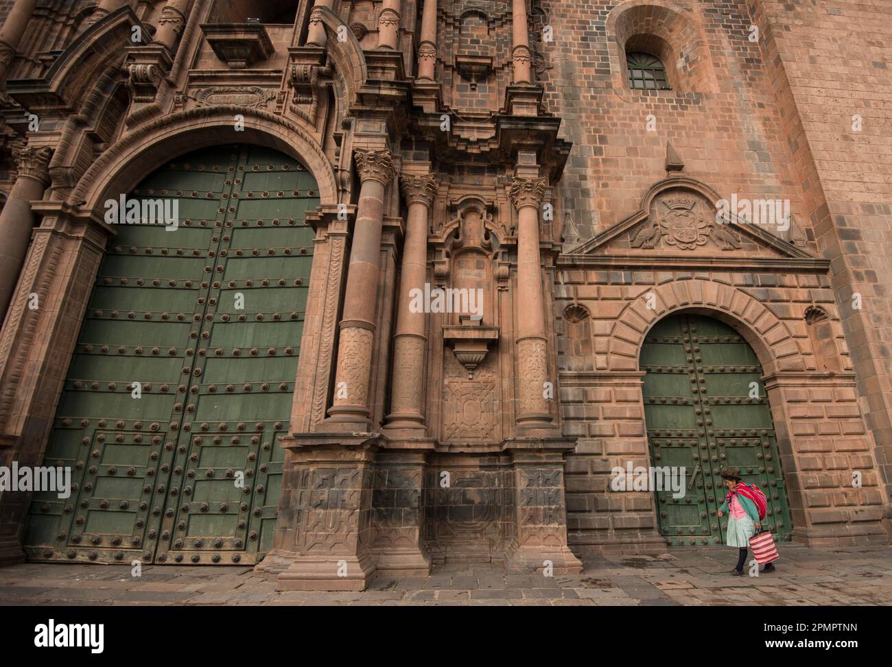 Donna cammina oltre le porte della Cattedrale di Cuzco; Cuzco, Perù Foto Stock