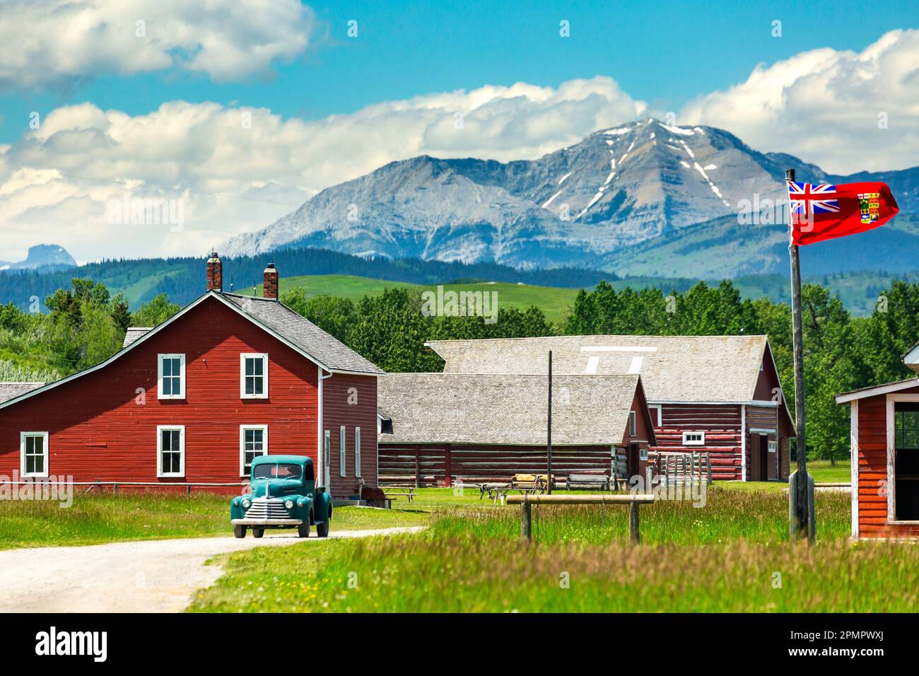 Sito storico con edifici dipinti di rosso, vecchio camion, colline pedemontane, montagne, cielo blu e nuvole sullo sfondo, a sud di Longview, Alberta Foto Stock