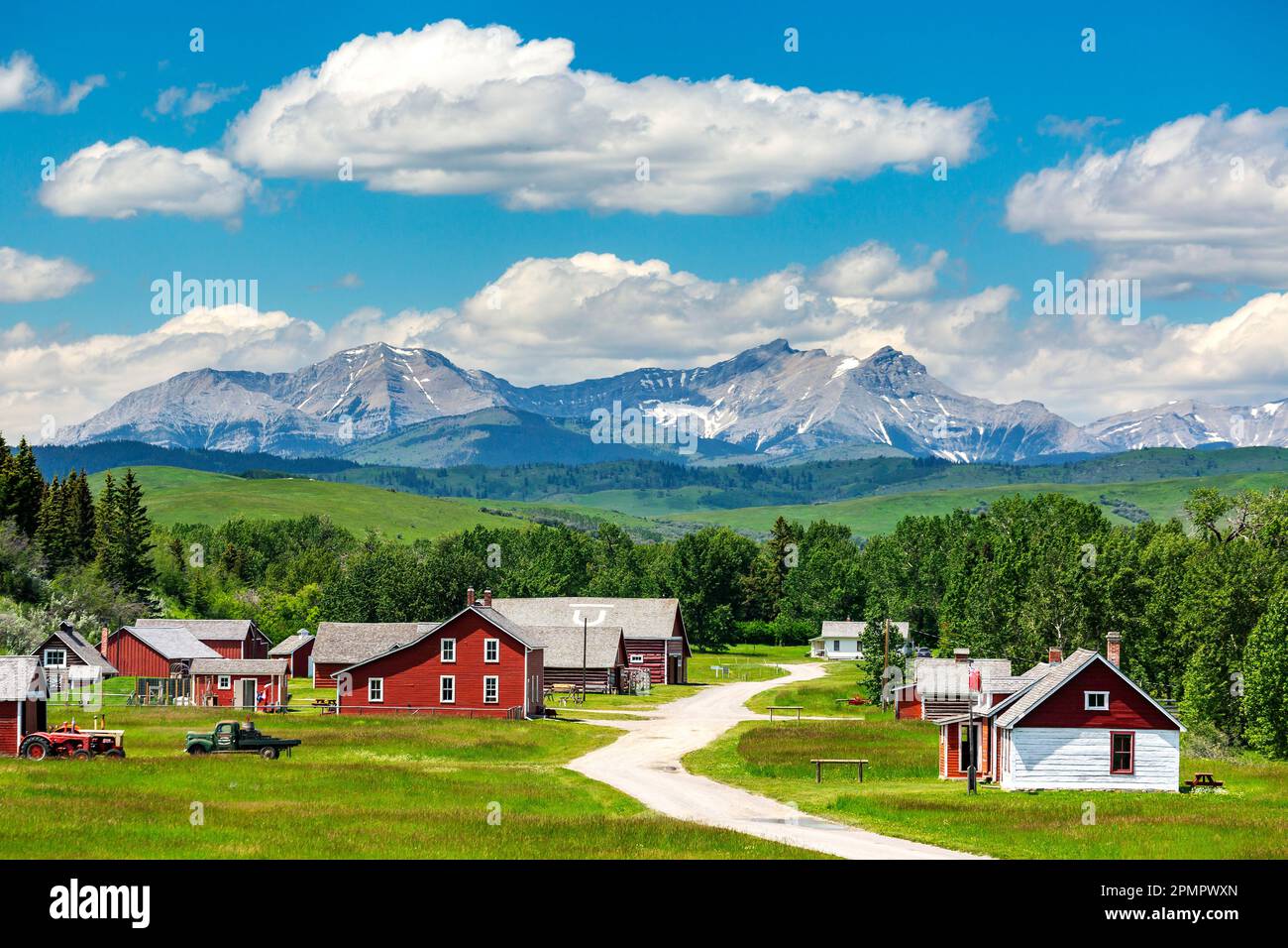 Sito storico con edifici dipinti di rosso, colline pedemontane, montagne, cielo blu e nuvole sullo sfondo, a sud di Longview, Alberta; Alberta, Canada Foto Stock