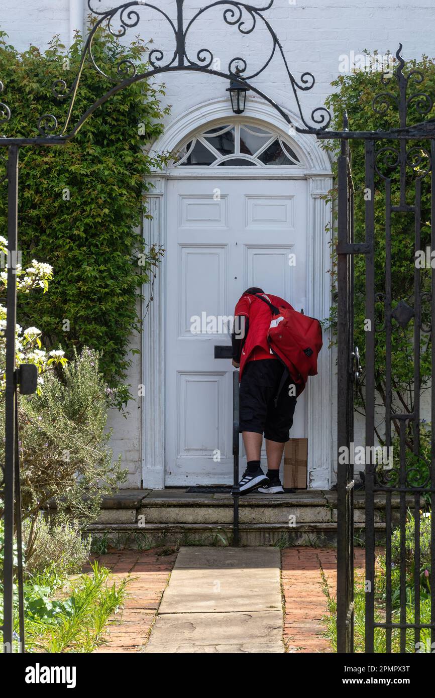 Postino alla porta d'ingresso di una proprietà che consegna posta e un pacchetto, Inghilterra, Regno Unito Foto Stock