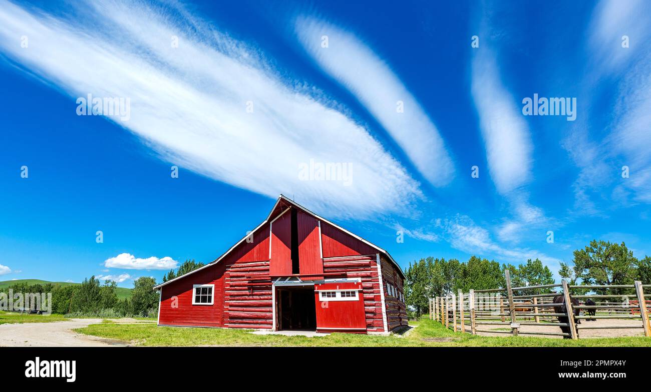 Storico fienile dipinto di rosso con recinzione in legno e nuvole spettacolari e cielo blu, a sud di Longview, Alberta; Alberta, Canada Foto Stock