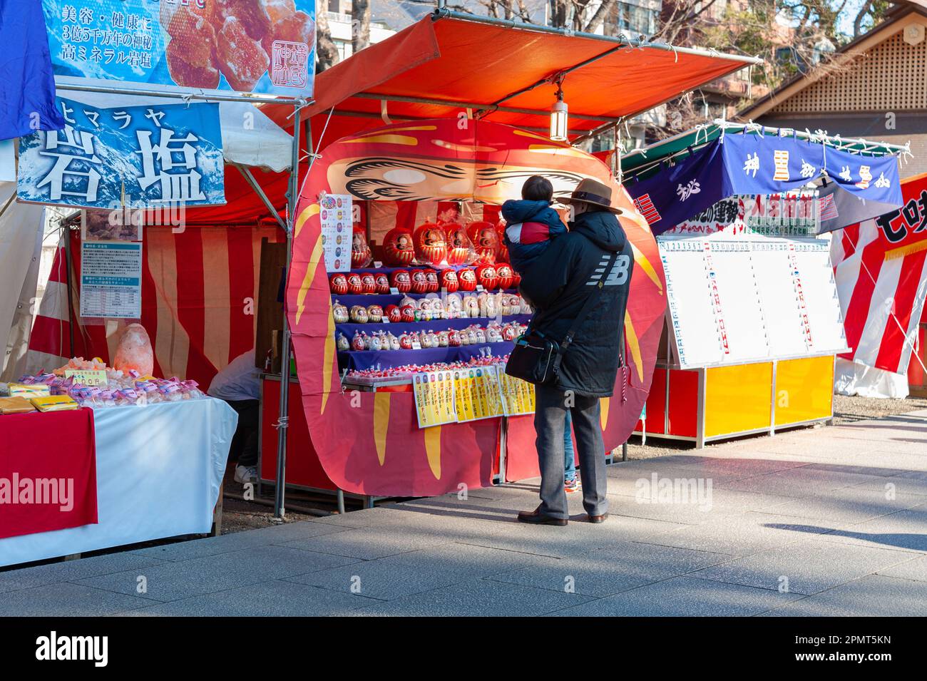 Chiyoda City, Tokyo, Giappone - 03 gennaio 2020: Padre con figlio in grembo che guarda le bambole Daruma in mostra presso uno stand di vendita. Foto Stock