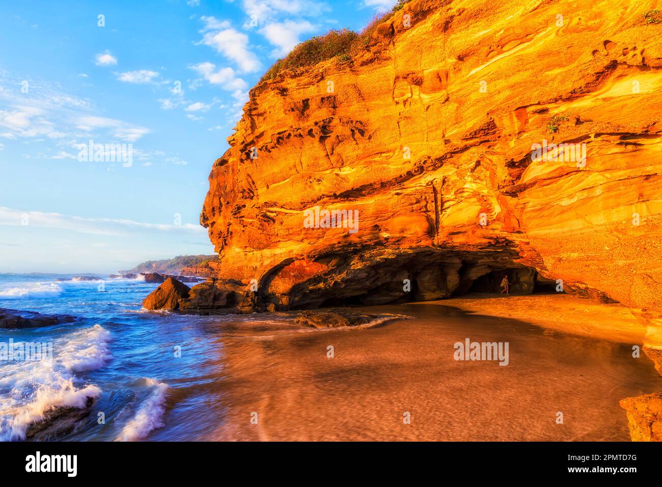 Ingresso alla grotta della spiaggia di cave erose, al largo della spiaggia di sabbia, con luce solare calda e soffusa - costa australiana del Pacifico. Foto Stock