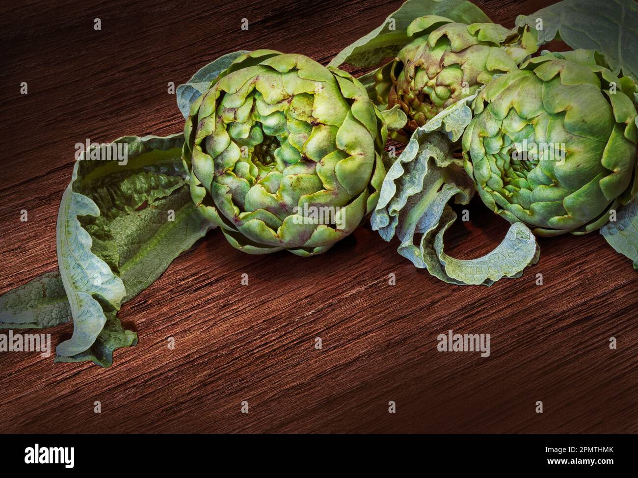 Carciofi biologici freschi raccolti con foglie su tavola di legno. Spazio di copia. Foto Stock