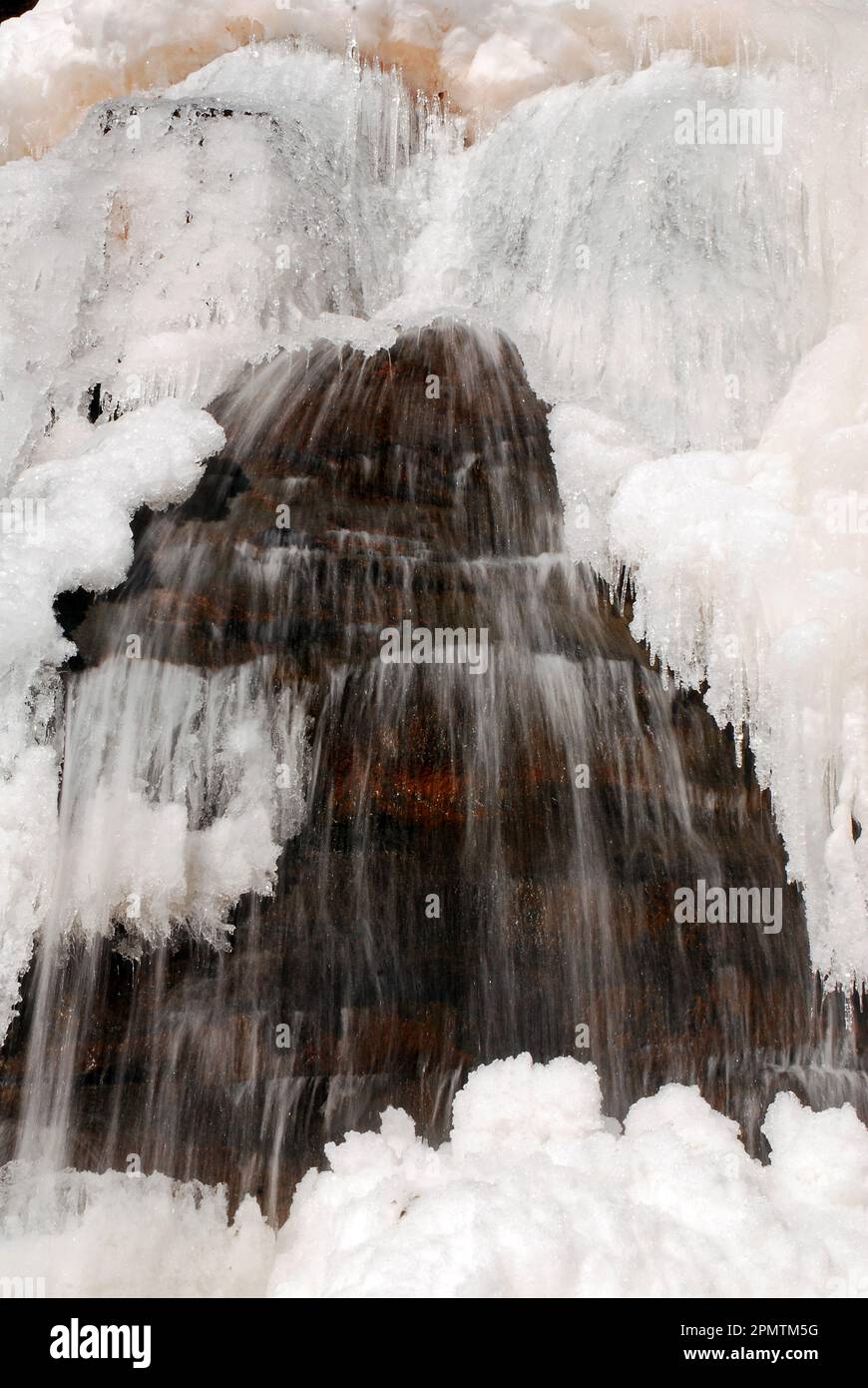Durante una fredda giornata invernale, l'acqua proveniente da una cascata continua a fluire, nonostante lo strato superficiale sia congelato Foto Stock