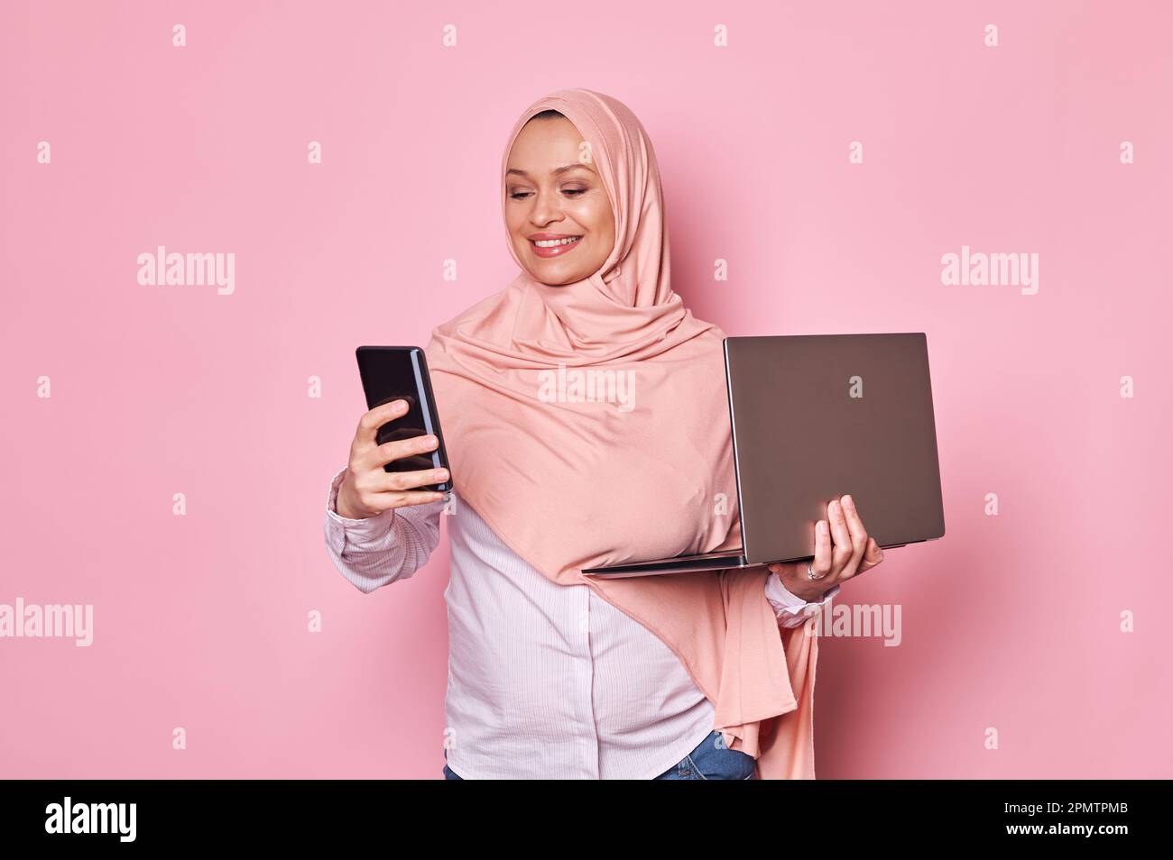 Donna araba musulmana, donna d'affari incinta in hijab rosa, con telefono cellulare e computer portatile. Gravidanza e carriera Foto Stock