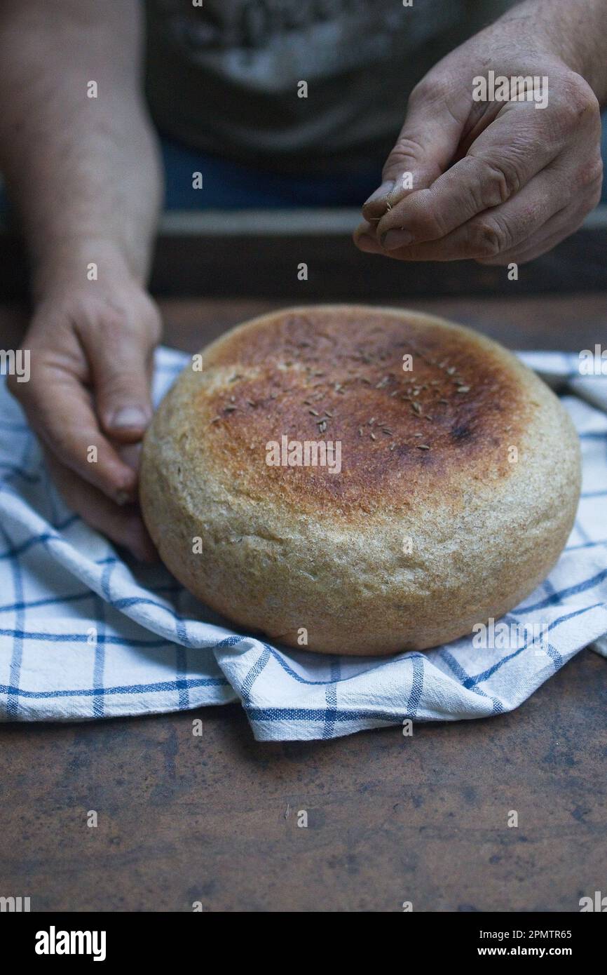 Crosta di pane fatta in casa su sfondo di legno. Panettiere che tiene il pane fresco nelle mani. Concetto di vita ferma. Atmosfera scura. Vista dall'alto Foto Stock