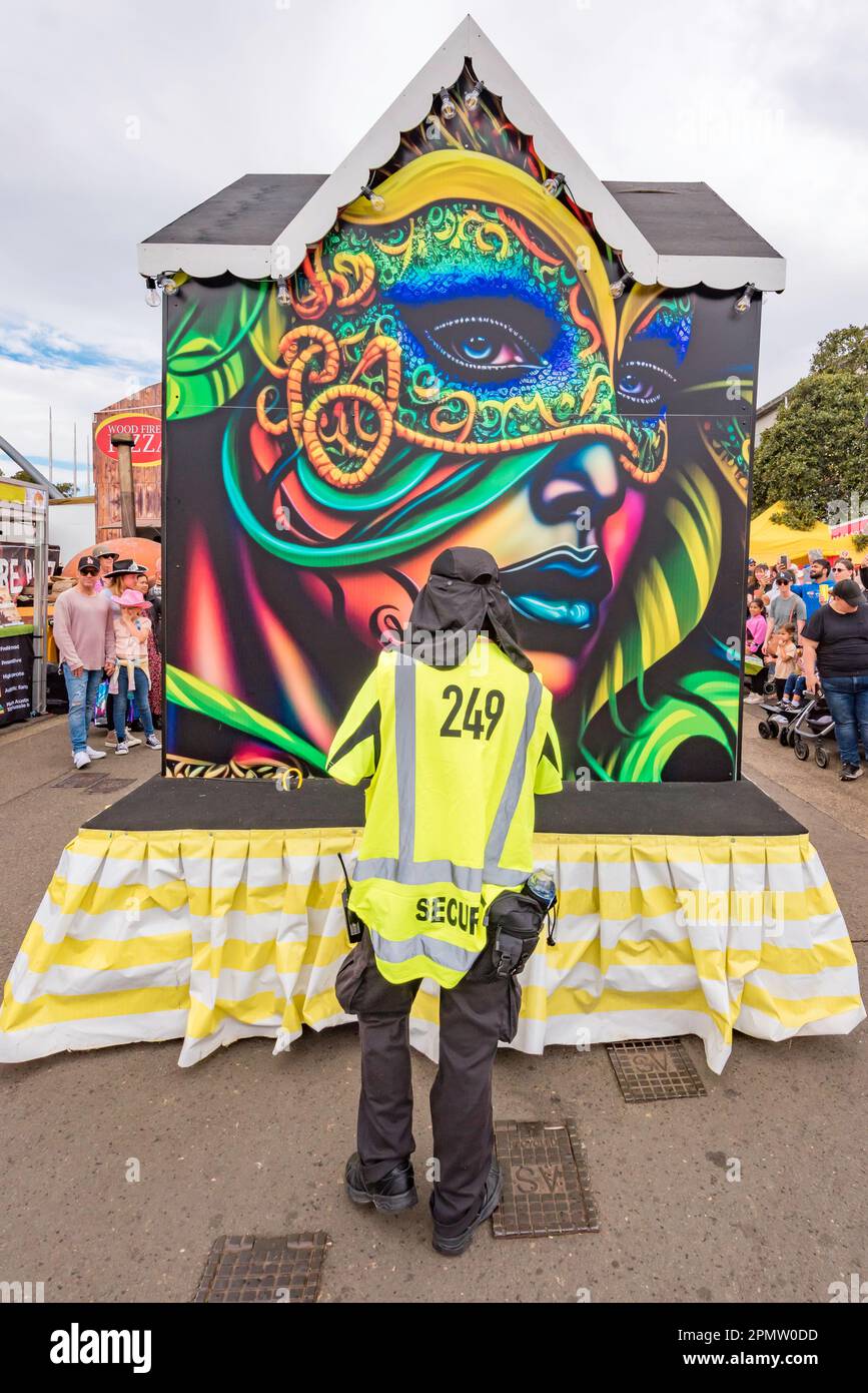 Un grande dipinto del volto di una donna colorata guarda in basso su una persona di sicurezza che cammina sul retro di una parata al Royal Easter Show 2023 di Sydney. Foto Stock