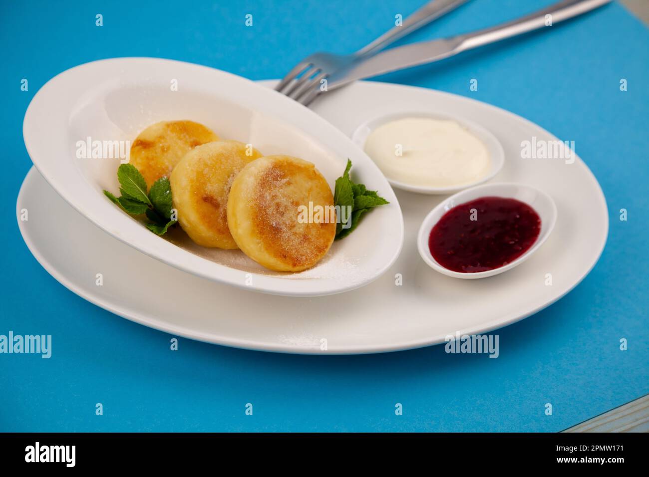 Frittelle di formaggio ricotta rotonda in un piatto bianco su sfondo blu. Cibo prima colazione. Cibo sano. Salsa di panna acida e menta. Primo piano vista dall'alto. Pasto dessert. Frittelle di ricotta al formaggio ricotta. Foto Stock