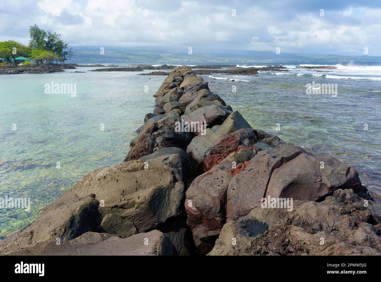Spiaggia hawaiana separata dall'oceano con una massiccia barriera rocciosa, incorniciata da un orizzonte oceano infinito e da nuvole ondulate sopra. Foto Stock