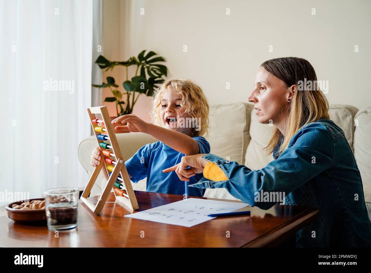 Madre e figlio studiano matematica con abaco per la classe scolastica all'interno della casa - concetto di famiglia e amore - Focus sulla faccia della mamma Foto Stock