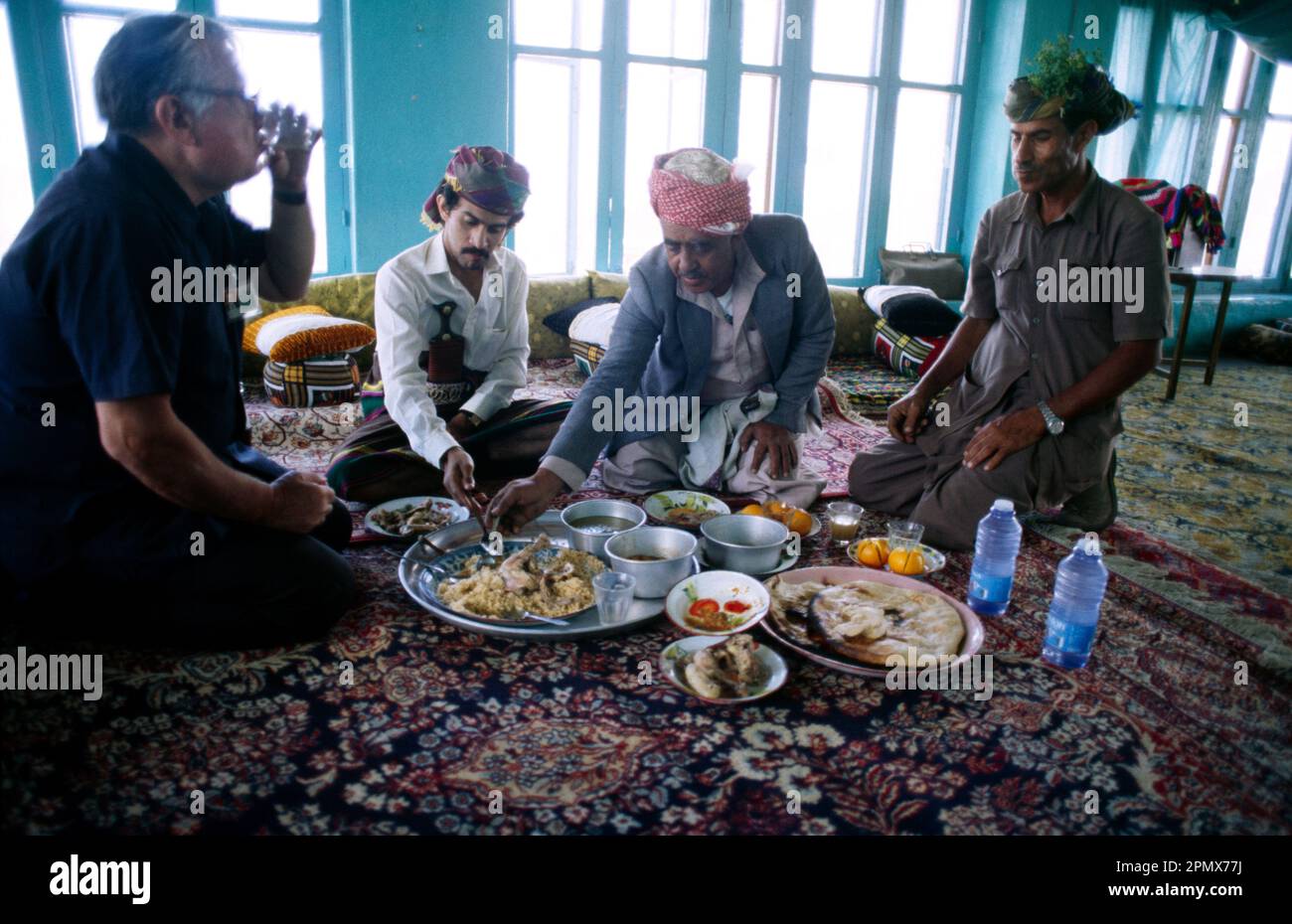 Yemen Muslim Men seduti al piano mangiare pasto con mani e accompagnatore che serve pasto agli ospiti Foto Stock