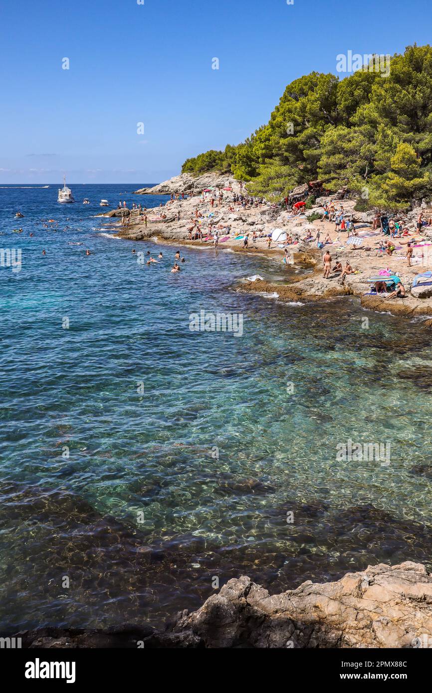 Pula, Croazia - 21 agosto 2022: Sovraffollata spiaggia rocciosa con mare Adriatico turchese durante le vacanze estive. Posto per vacanze soleggiato verticale. Foto Stock