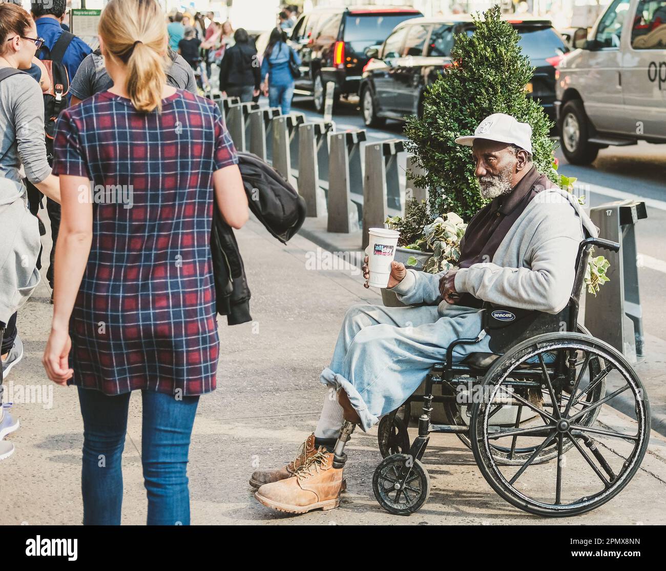 L'uomo disabile ha visto chiedere carità mentre si siede sulla sua sedia a rotelle mentre la gente cammina oltre. L'uomo può essere visto con una gamba inferiore sinistra artificiale. Foto Stock