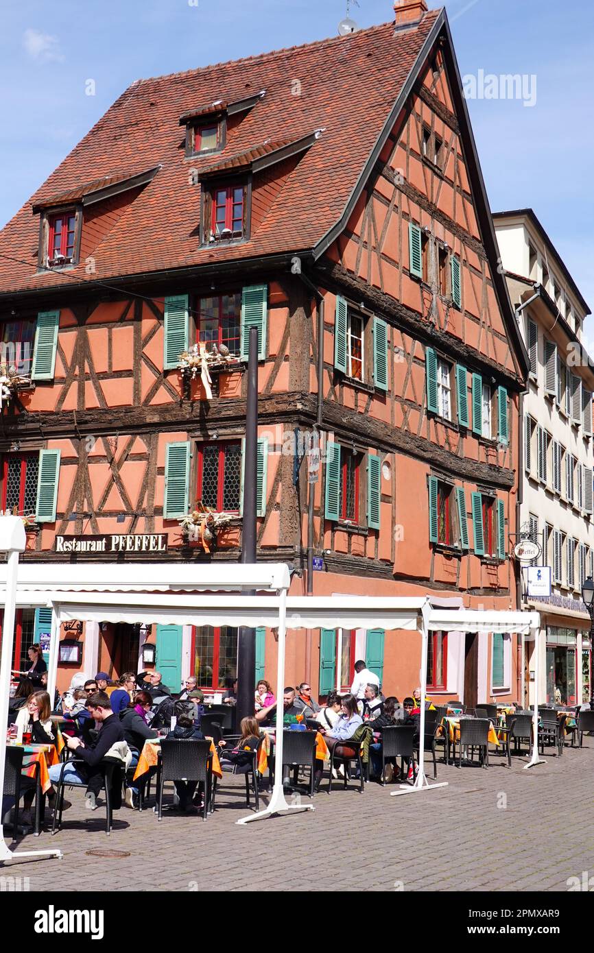 Persone sedute fuori, in una giornata di sole primaverile, a mangiare al ristorante Wistub 'PFEFFEl', nel cuore di Colmar, Alsazia, Francia. Foto Stock