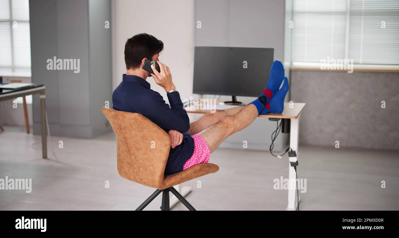 Vestiti con divertenti Shorts alla scrivania dell'ufficio. Chiamata telefonica Foto Stock