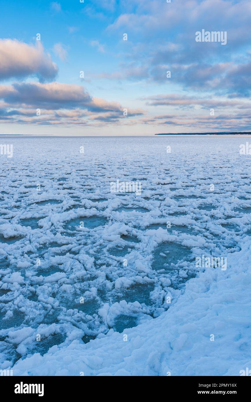 Un sereno paesaggio invernale di un lago ghiacciato in Svezia, circondato da cieli azzurri e nuvole innevate. La tranquillità regna senza persone o onde di vento Foto Stock