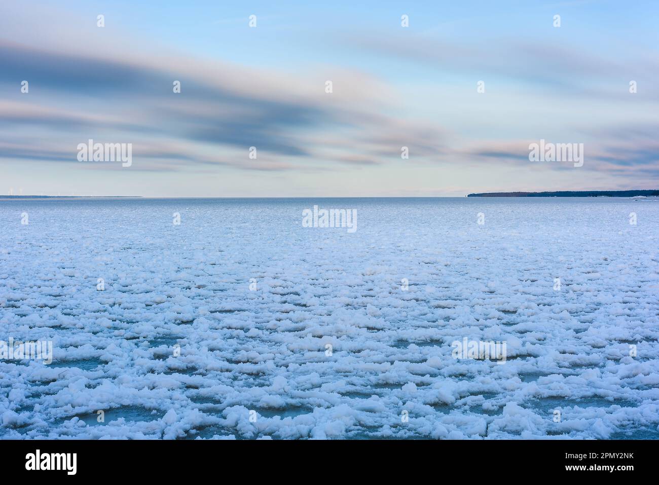 Un sereno paesaggio invernale di un lago ghiacciato in Svezia, circondato da cieli azzurri e nuvole innevate. La tranquillità regna senza persone o onde di vento Foto Stock