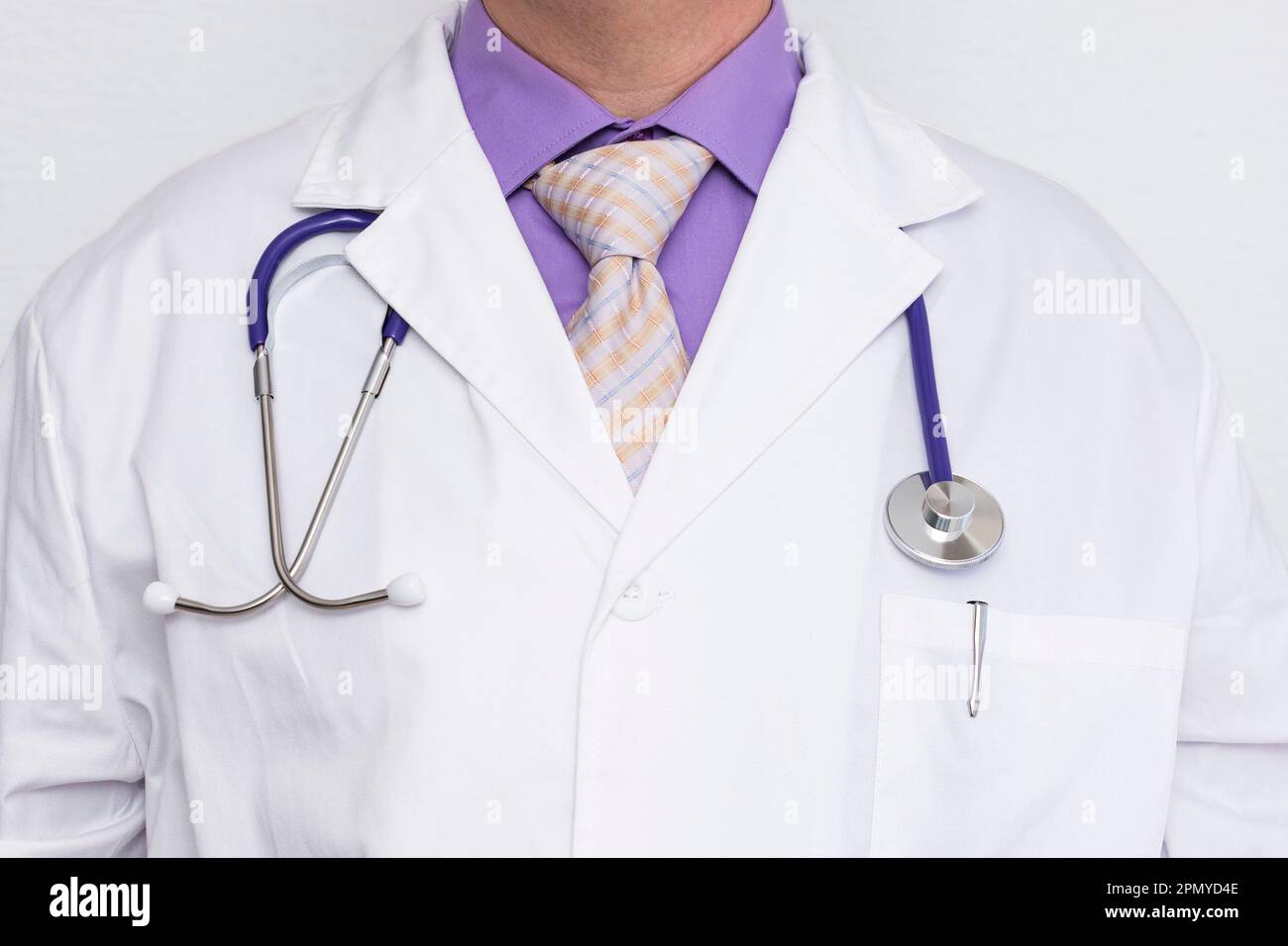Primo piano del petto di un medico caucasico irriconoscibile che indossa un cappotto bianco sopra una camicia viola e una cravatta. Uno stetoscopio pende dal collo e dalla pe Foto Stock