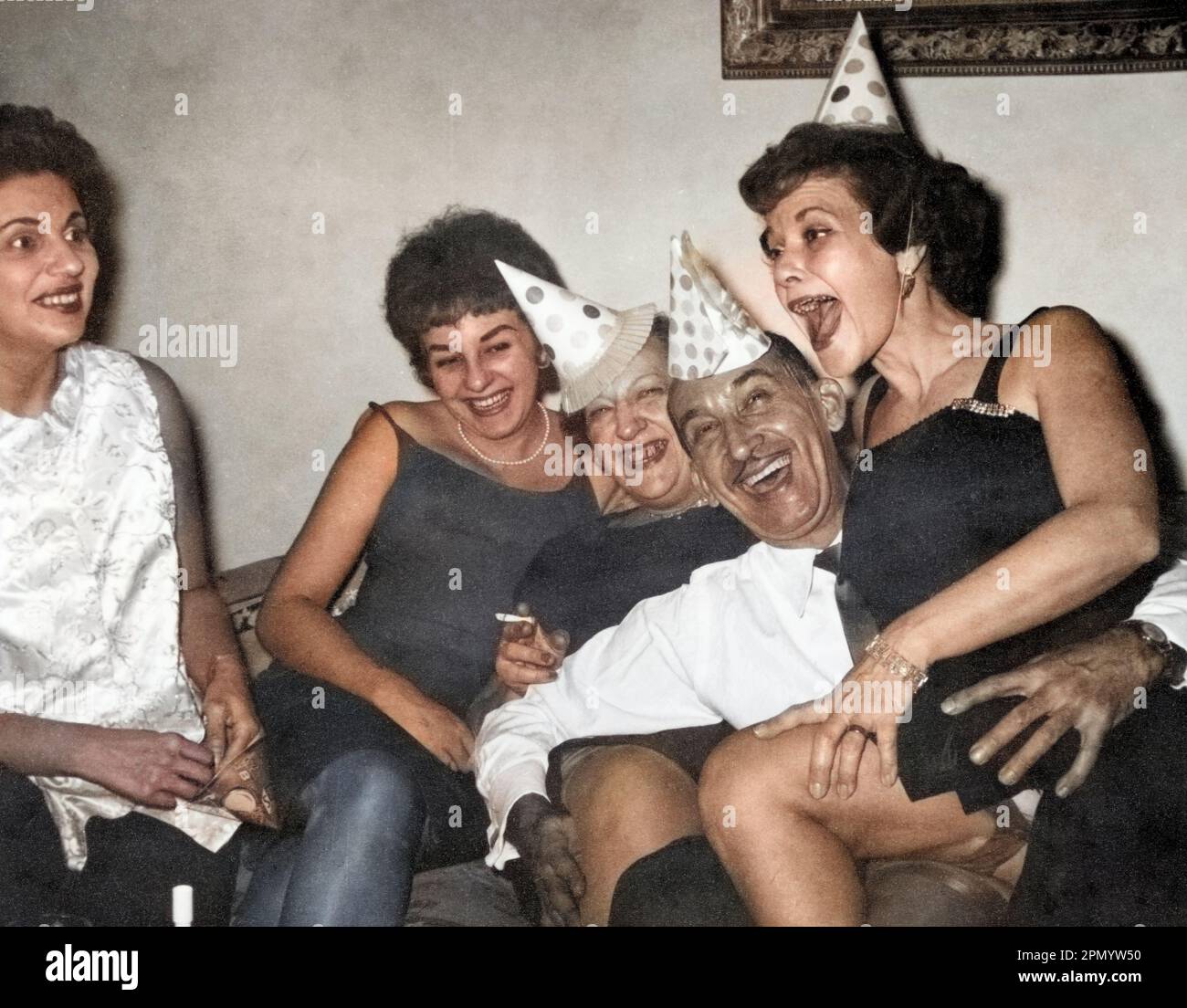 Circa 1960: adulti che festeggiano a casa con cappelli da festa, USA.; fotografia vintage colorata. Foto Stock