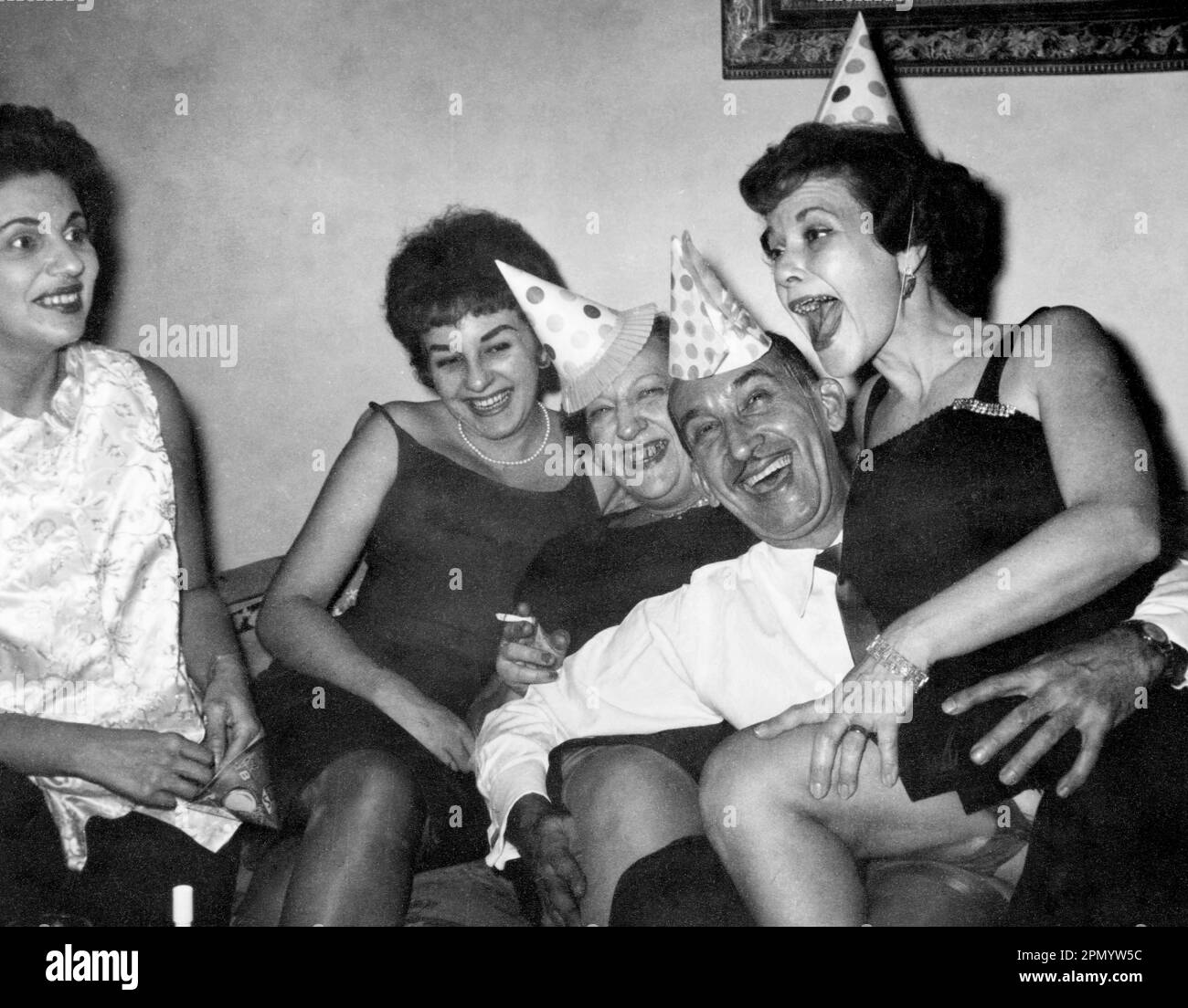 Circa 1960: adulti che festeggiano a casa con cappelli da festa, USA., originale fotografia vintage in bianco e nero. Foto Stock